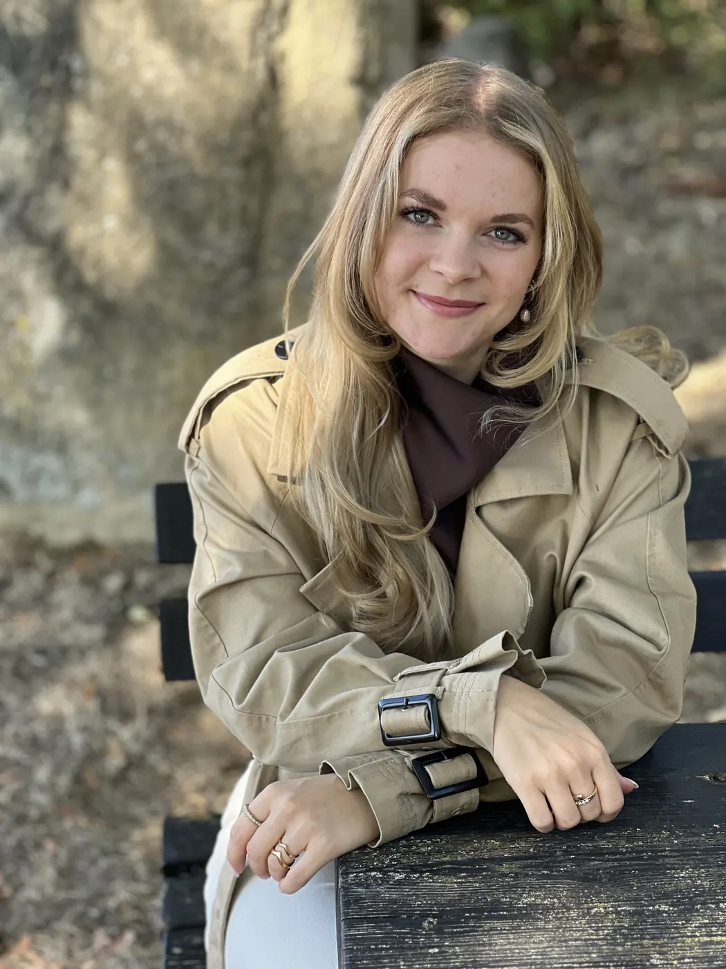 Rachel Ellerbeck im Trenchcoat auf einer Holzbank